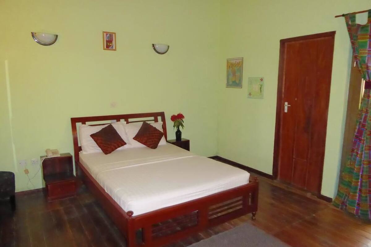 A bedroom with a wooden bed, a nightstand, a wall-mounted lamp, and a door.