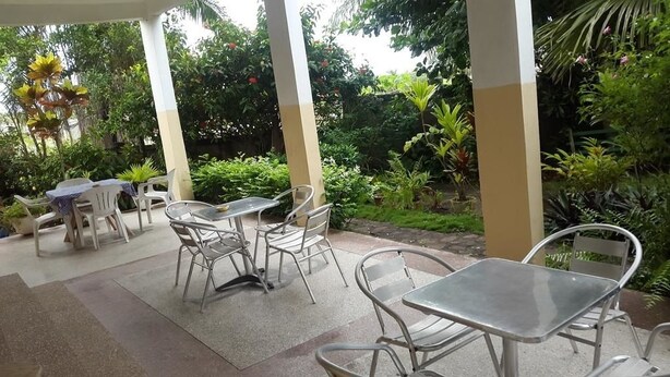 Un patio al aire libre con mesas y sillas de metal, rodeado de abundante vegetación y plantas.