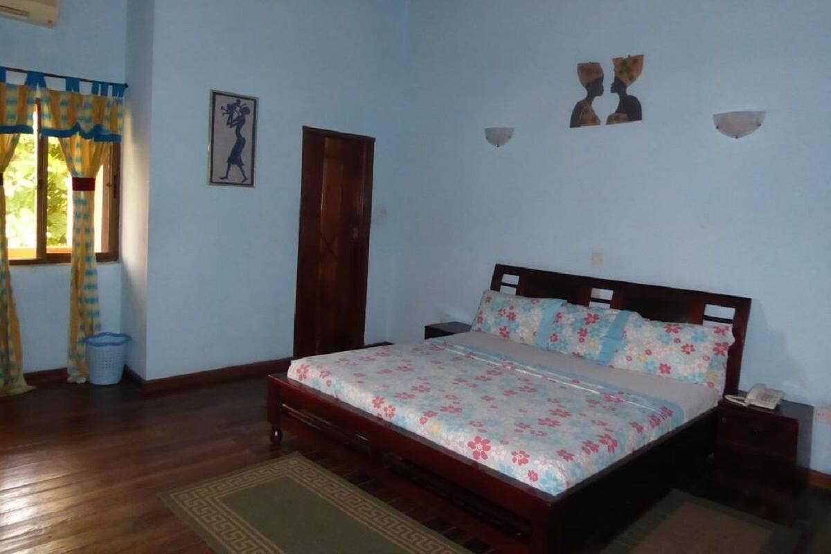 A bedroom with a wooden bed, a nightstand, a wall-mounted lamp, and a window with curtains.