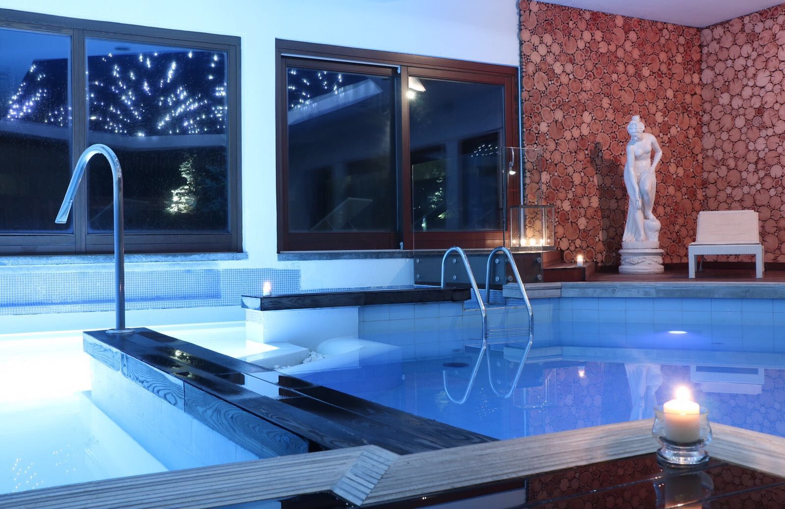Ein Schwimmbecken mit Glasrand, einer Statue und einer Nachttraumsicht durch die Fenster.