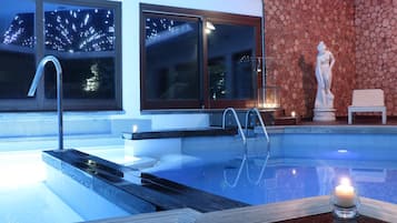 Ein Schwimmbecken mit Glasrand, einer Statue und einer Nachttraumsicht durch die Fenster.