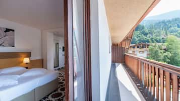 Habitación de hotel con cama, un cuadro y un balcón con vistas a una montaña boscosa.