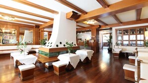 A spacious room with wooden beams, a central fireplace, and multiple tables with white tablecloths. - Olympic Royal (Giustino)