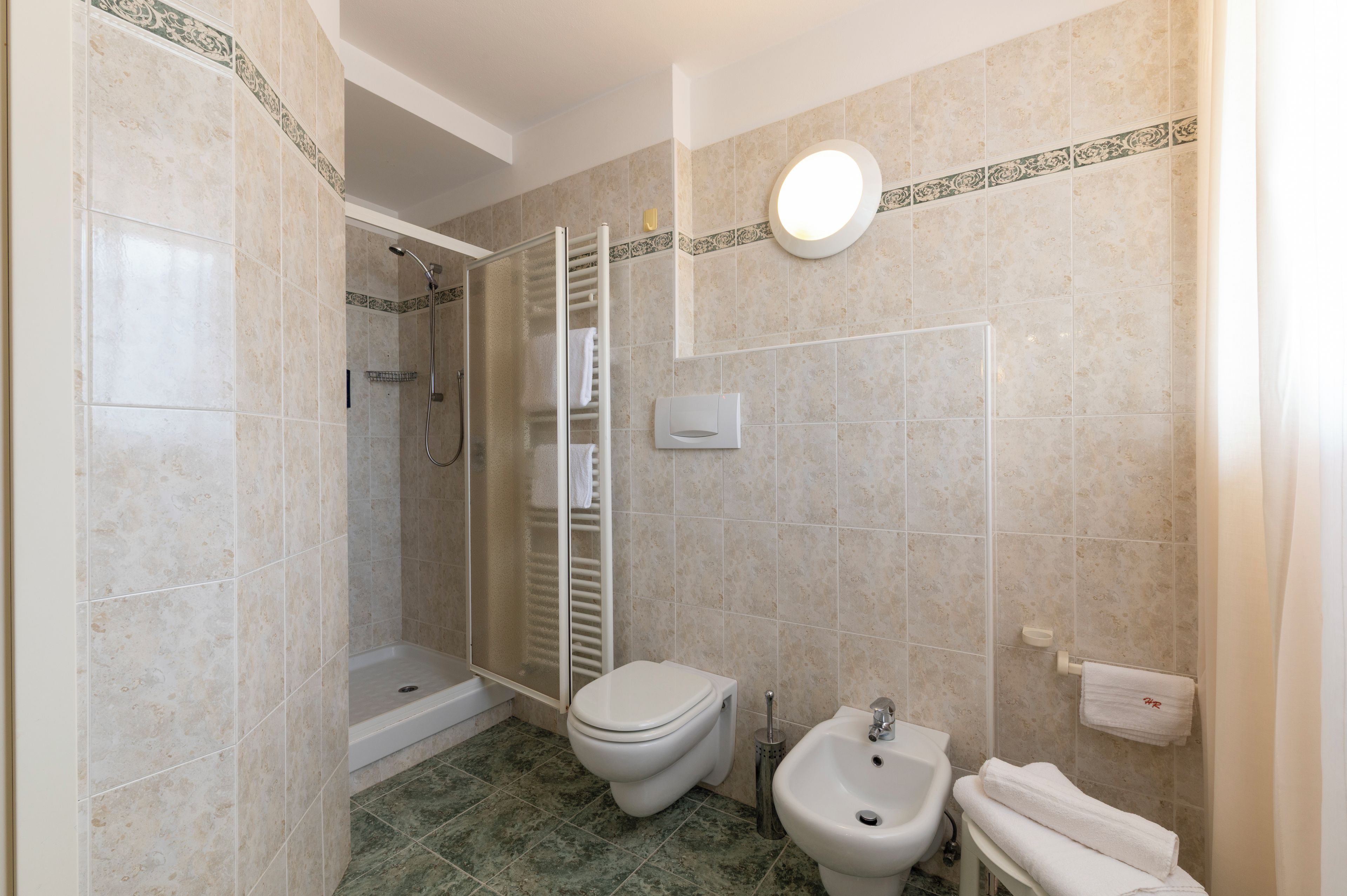 Un baño con ducha, inodoro, bidé y un perchero para toallas.