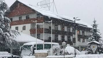 Un hotel dal tetto rosso con numerose finestre, immerso in alberi coperti di neve e circondato da auto parcheggiate.
