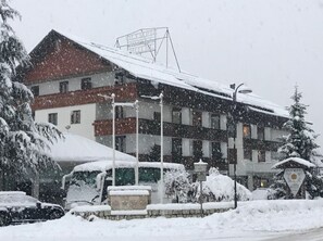 A hotel with a red roof and multiple windows, surrounded by snow-covered trees and parked cars. - Olympic Royal (Giustino)