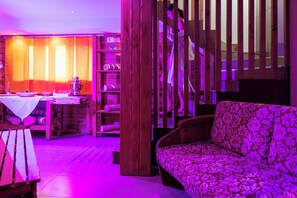 A room with a wooden sofa, a dining table with chairs, and a wooden bookshelf. - Olympic Royal (Giustino)