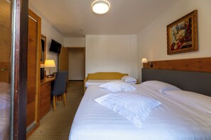 A hotel room with a bed, desk, chair, television, and a painting on the wall. - Olympic Royal (Giustino)