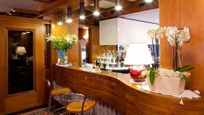 A bar area with wooden paneling, a mirror, and two chairs. There are vases with flowers and a lamp on the counter. - Olympic Royal (Giustino)
