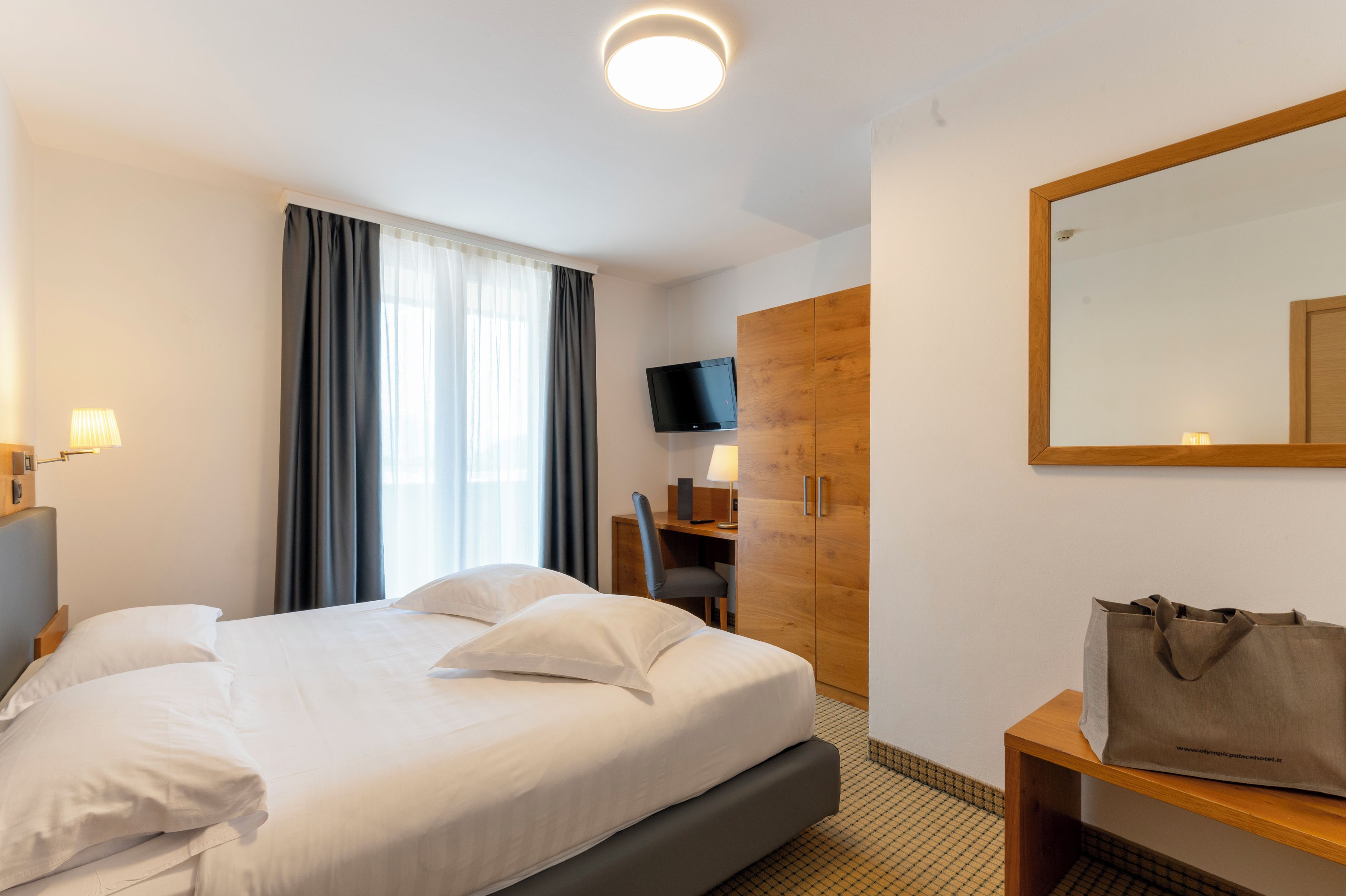 Hotellihuone, jossa on sänky, työpöytä, tuoli, televisio ja vaatekaappi.