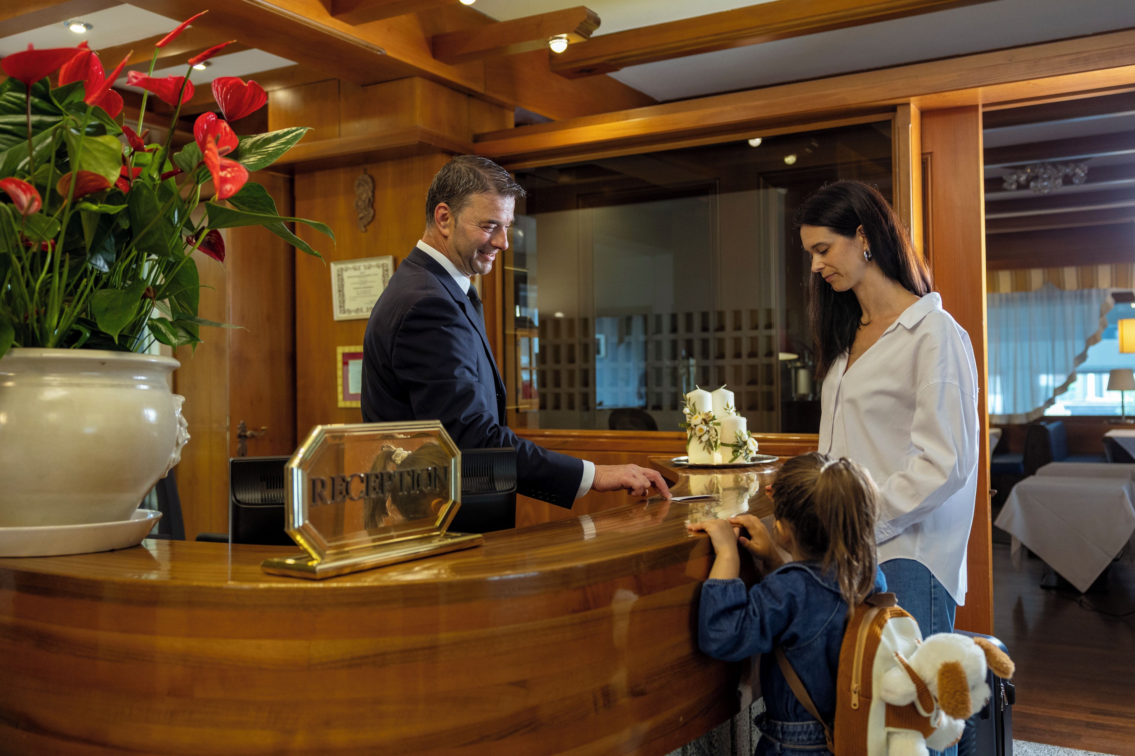 A hotel reception desk with a receptionist, a guest, and a child.