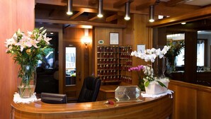 A reception desk with a wooden finish, a black leather chair, and a sign that reads "RECEPTION". - Olympic Royal (Giustino)