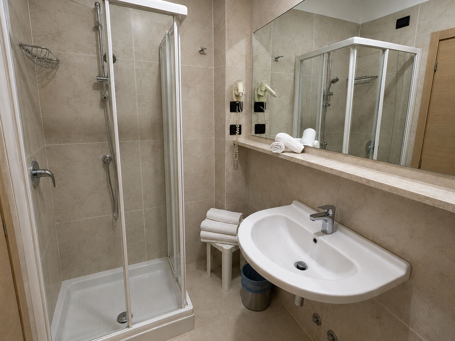 Een moderne badkamer met een douche in een glazen cabine, een witte wastafel en een spiegel boven de wastafel.