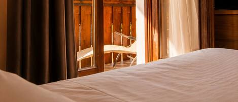 Una habitación de hotel con cama, cortinas y vistas a un balcón con una silla.