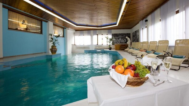 A swimming pool with a table of fruit and wine glasses in the foreground. - Olympic Royal (Giustino)