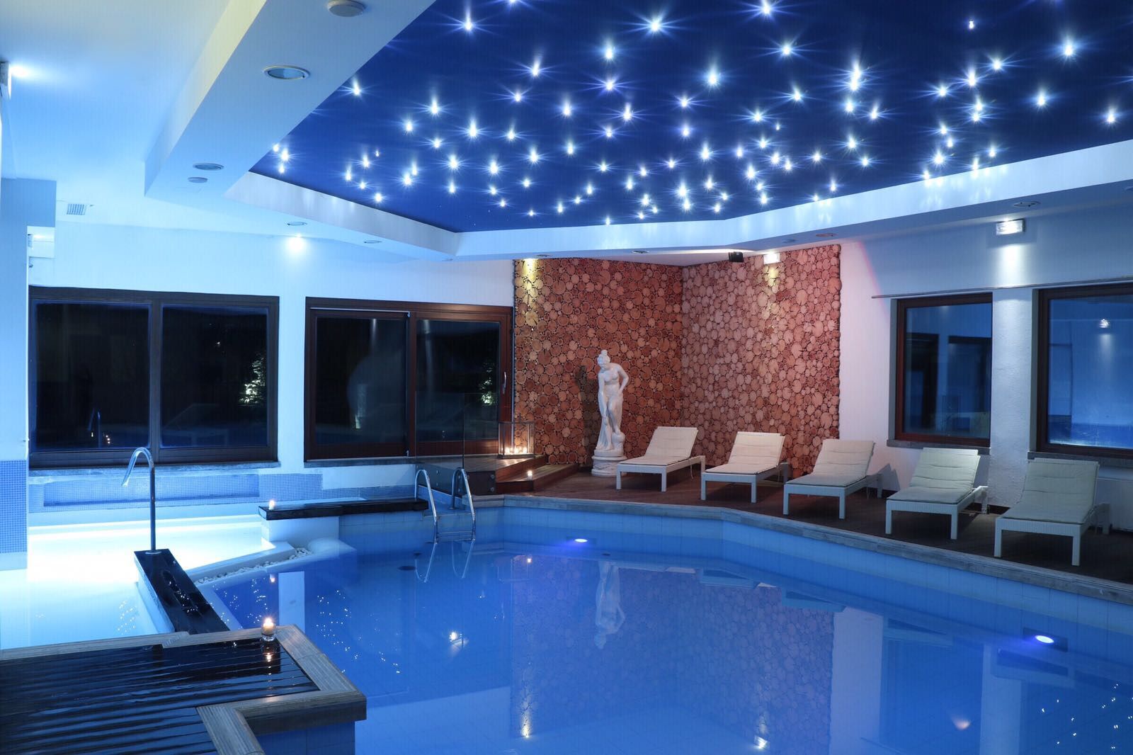 Una piscina interna con un soffitto decorato con un design che ricorda le stelle, una statua e poltrone relax.