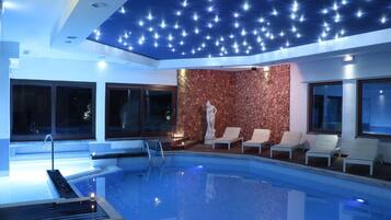 Una piscina interna con un soffitto decorato con un design che ricorda le stelle, una statua e poltrone relax.