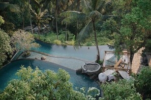 A serene pool area surrounded by lush greenery and palm trees, with a stone bridge and a small waterfall feature. - Bucu View Resort (Ubud)