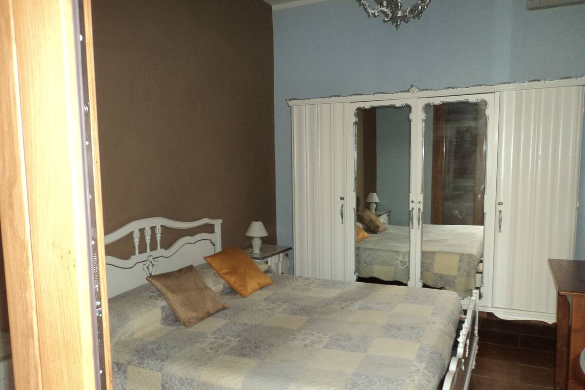 A bedroom with a bed, a nightstand, a lamp, and a wardrobe.