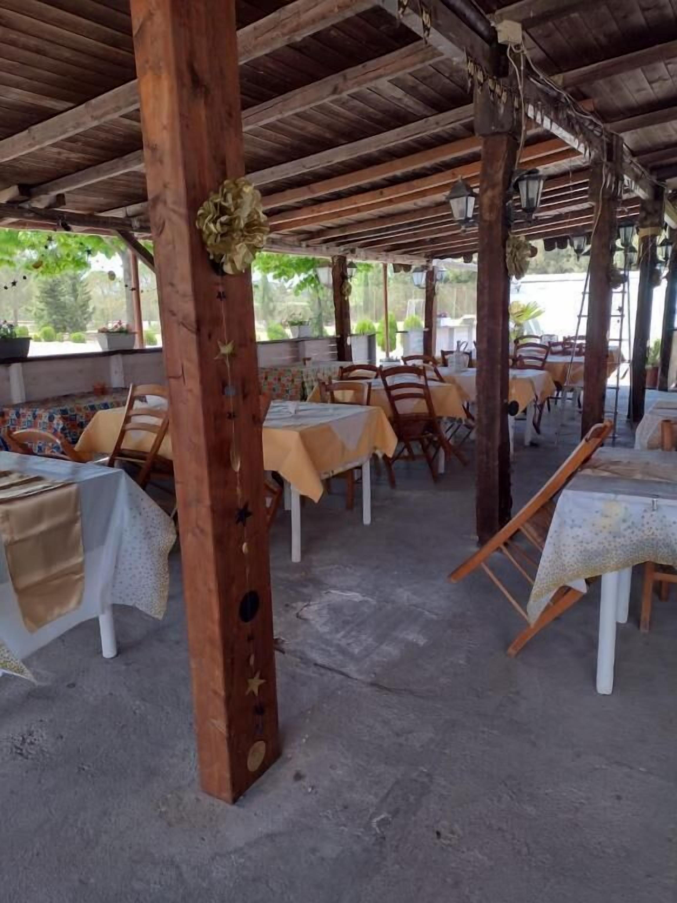 An outdoor dining area with tables and chairs, wooden pillars, and a covered roof.