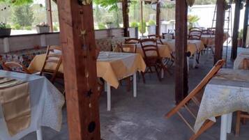 Un área de comedor al aire libre con mesas y sillas, pilares de madera y un techo cubierto.