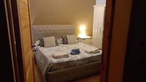 Un dormitorio con cama, almohadas, una mesita de noche y una lámpara.