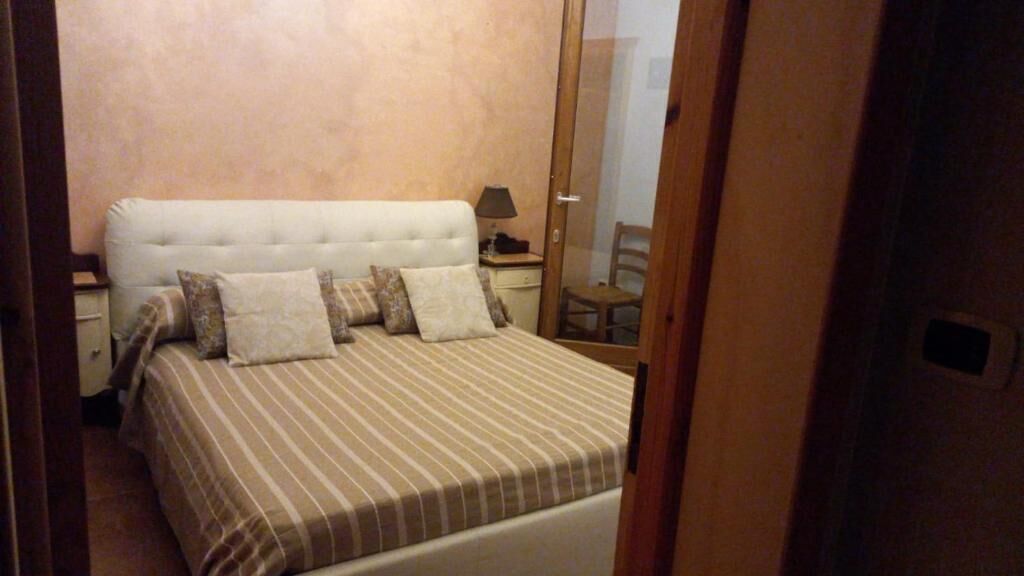 A bedroom with a bed, pillows, a nightstand, a lamp, and a chair.