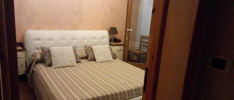 A bedroom with a bed, pillows, a nightstand, a lamp, and a chair.