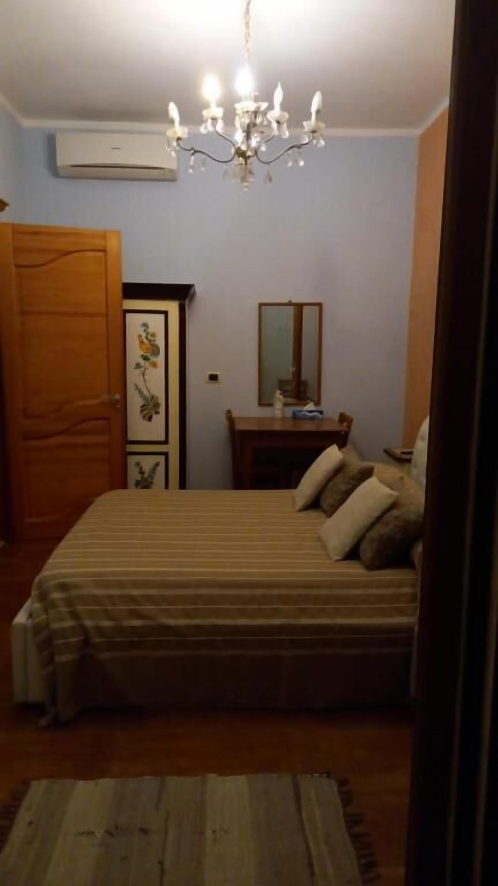 Ein Schlafzimmer mit einem Bett, einer Holztür, einem Schminktisch, einem Spiegel und einer Chandelier.