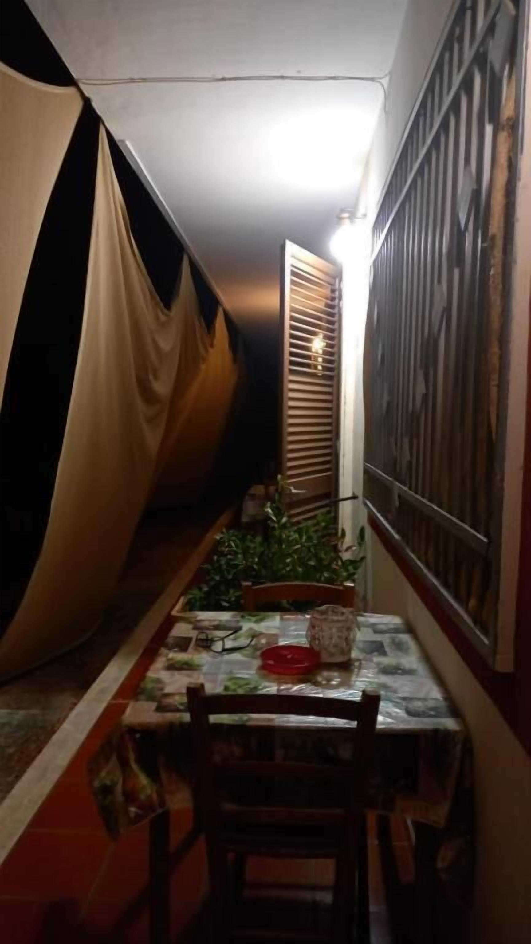 Un pasillo estrecho con una mesa y sillas, una ventana con persianas y una verja metálica.