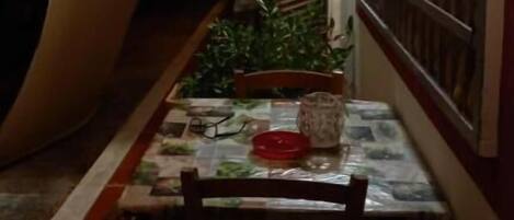 Un pasillo estrecho con una mesa y sillas, una ventana con persianas y una verja metálica.