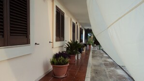Un pasillo con suelo de baldosas, plantas en macetas y un toldo blanco.