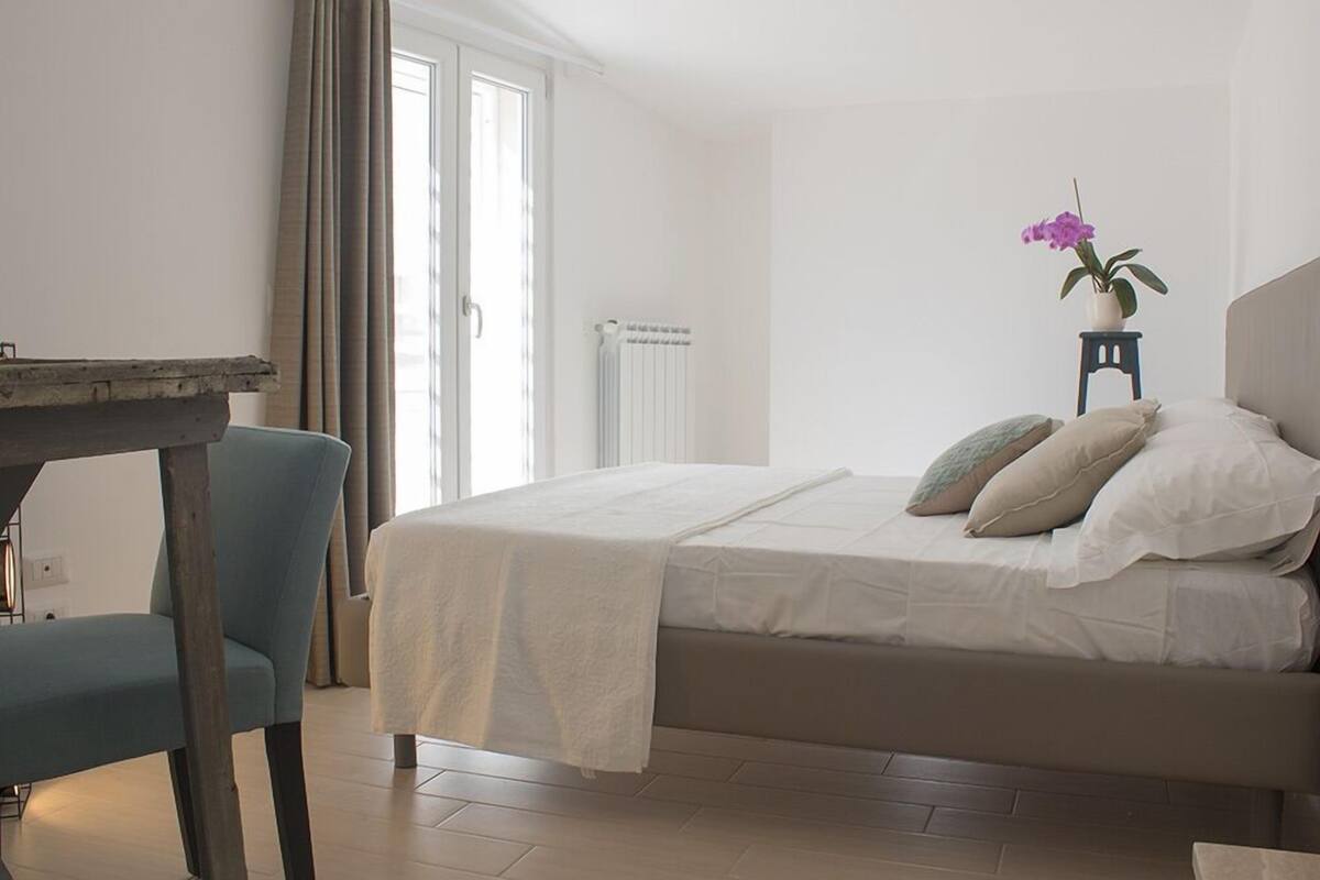 A bedroom with a bed, a chair, a table, and a potted plant.
