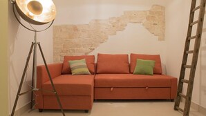 Una habitación con un sofá para dos personas, una lámpara de pie, una pared de piedra y una escalera de madera.