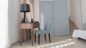 Un dormitorio con una cama, una silla, un escritorio con lámpara y una puerta.