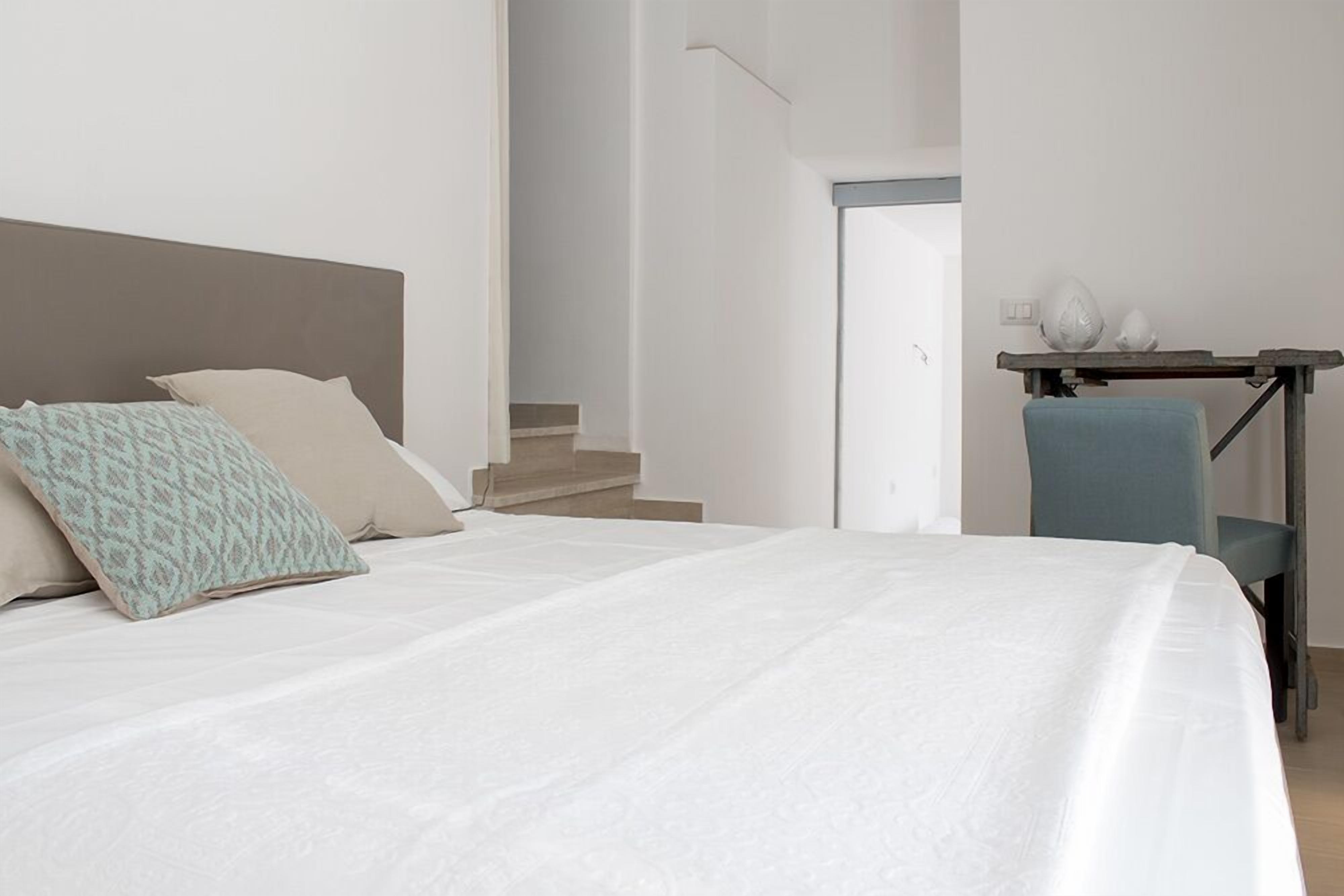 Une chambre à coucher avec un lit, des oreillers, une chaise et un bureau avec une lampe.