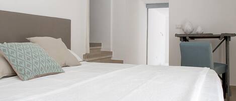 Une chambre à coucher avec un lit, des oreillers, une chaise et un bureau avec une lampe.