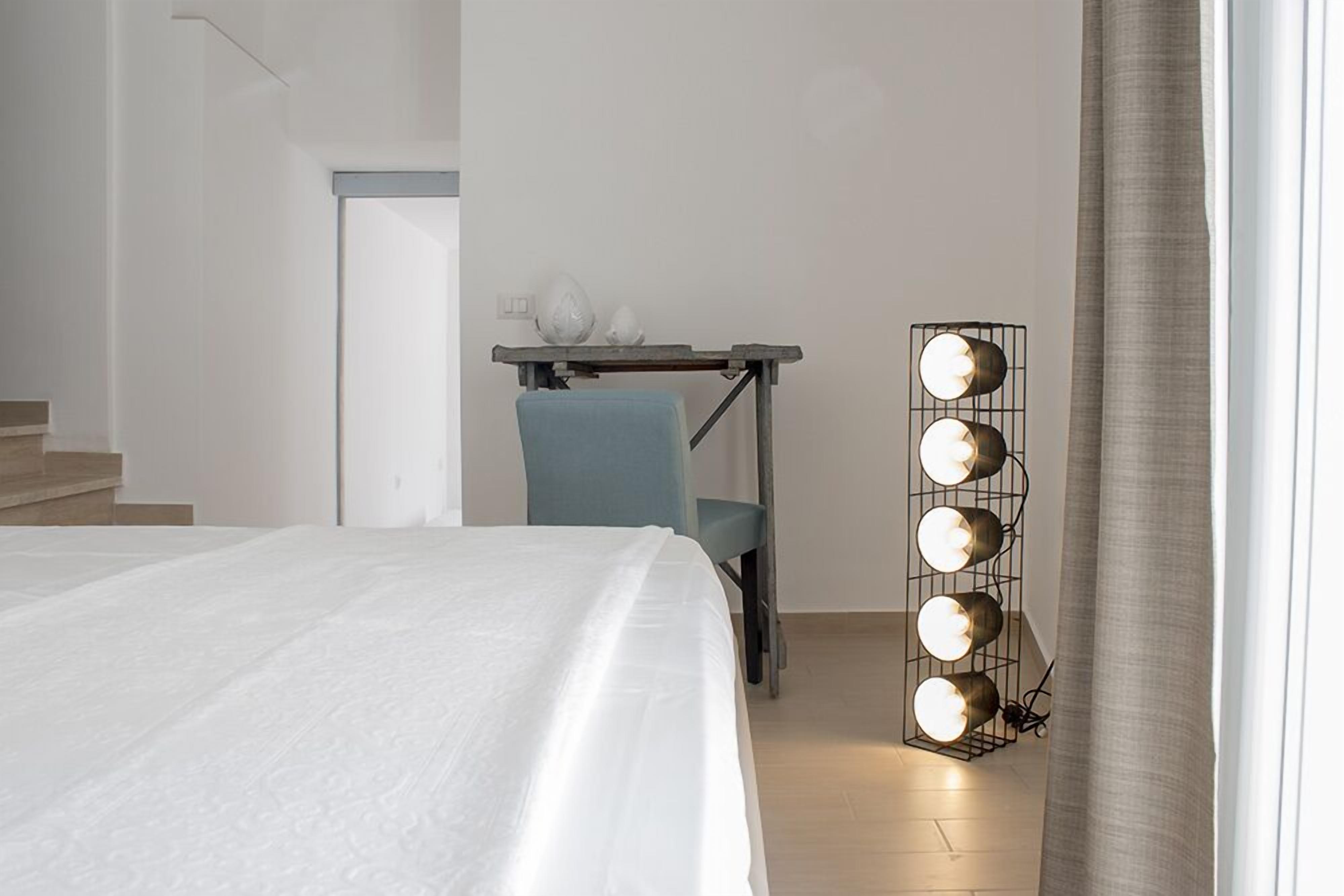 A hotel room with a bed, a chair, a desk with a lamp, and a staircase.