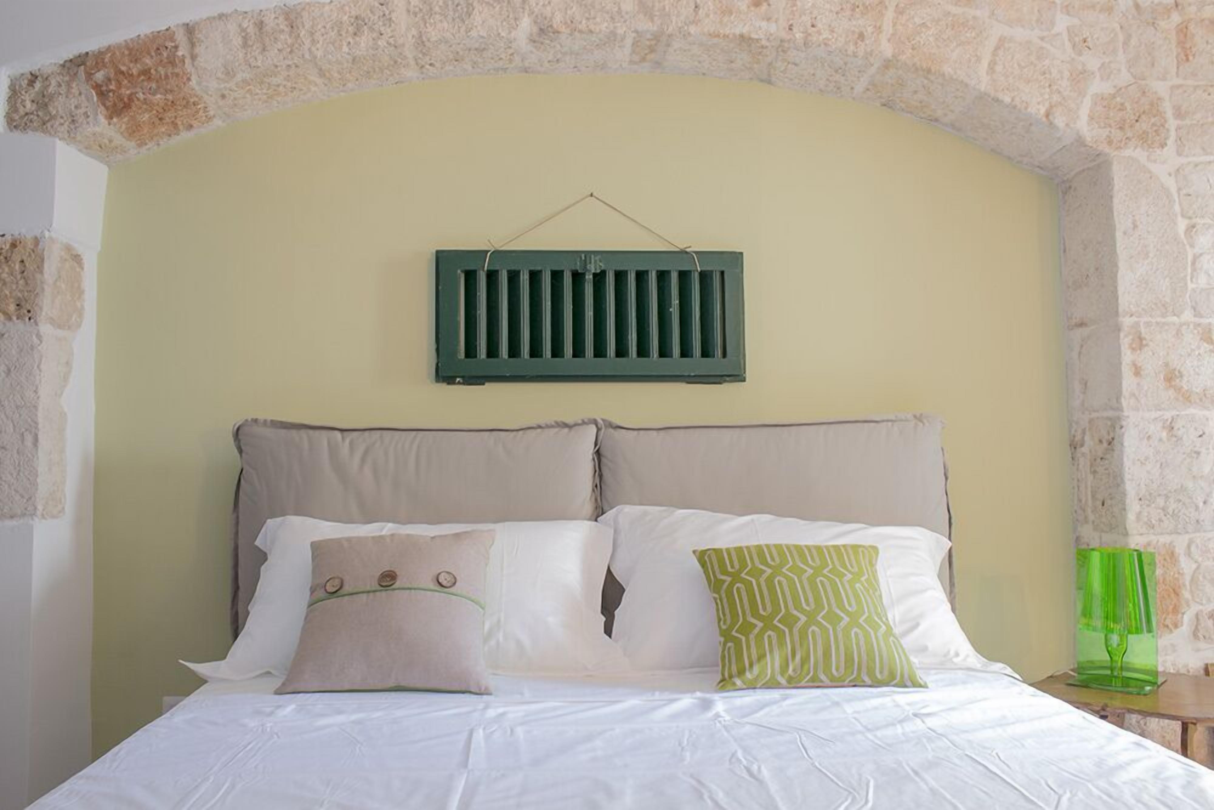 A bed with white bedding, beige and green pillows, and a green headboard.