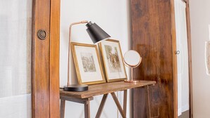 Un escritorio de madera con una lámpara de escritorio negra, dos cuadros enmarcados y un espejo redondo.