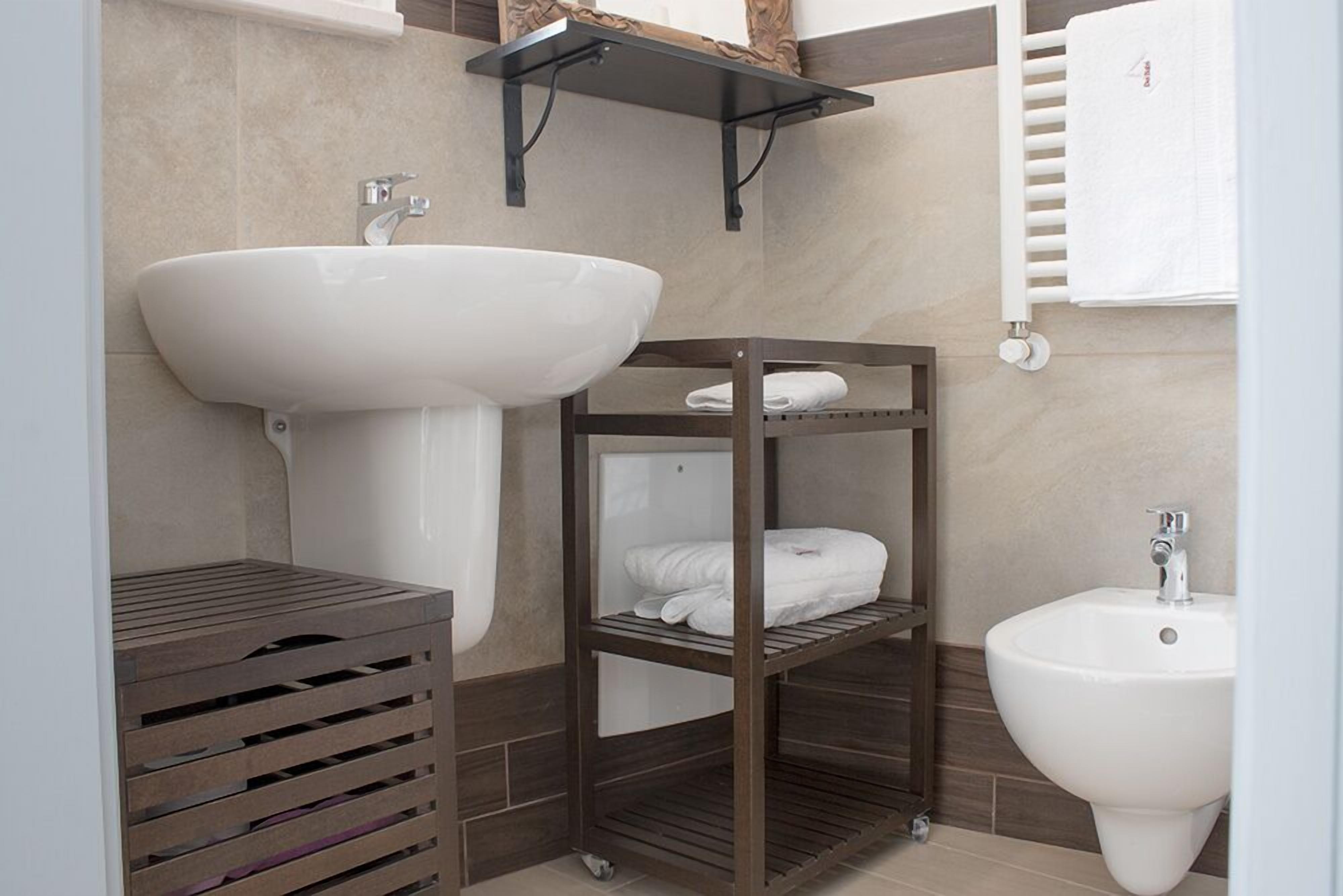 Un baño con un lavamanos grande, un inodoro pequeño y una estantería de madera con toallas.