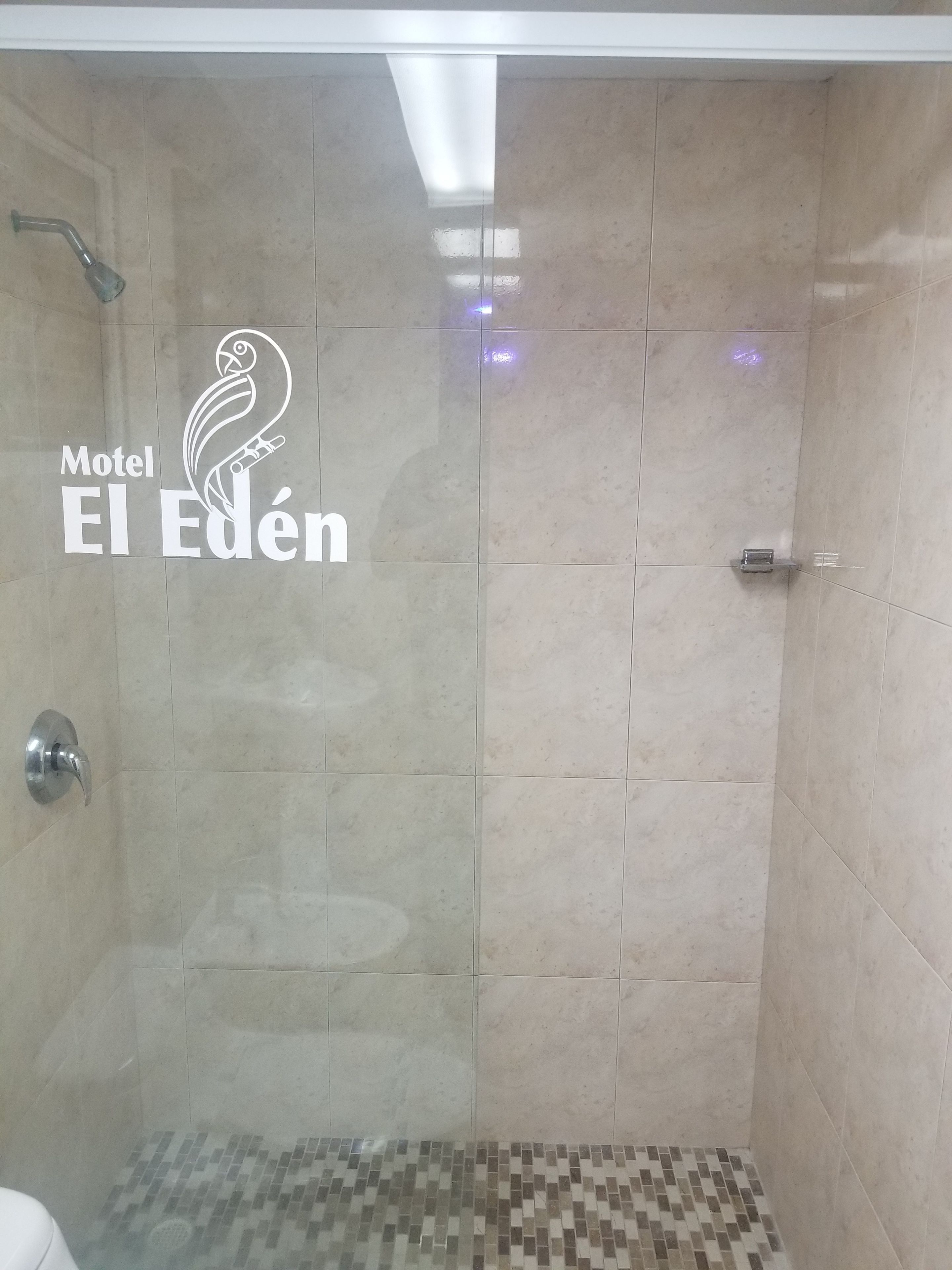 A shower area with a tiled wall and a logo for Motel El Eden.