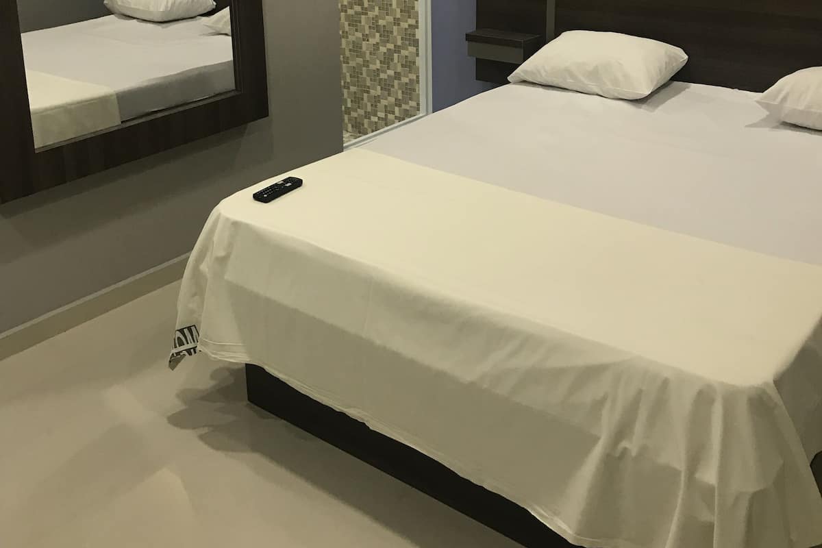 A modern bedroom with a large bed, a bedside table, a mirror, and a wall with a geometric tile pattern.