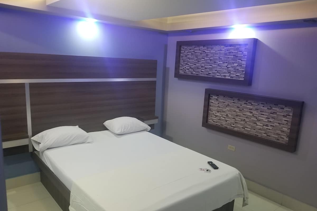 A neatly made bed with white linens, a wooden headboard, and a remote control on the bed.