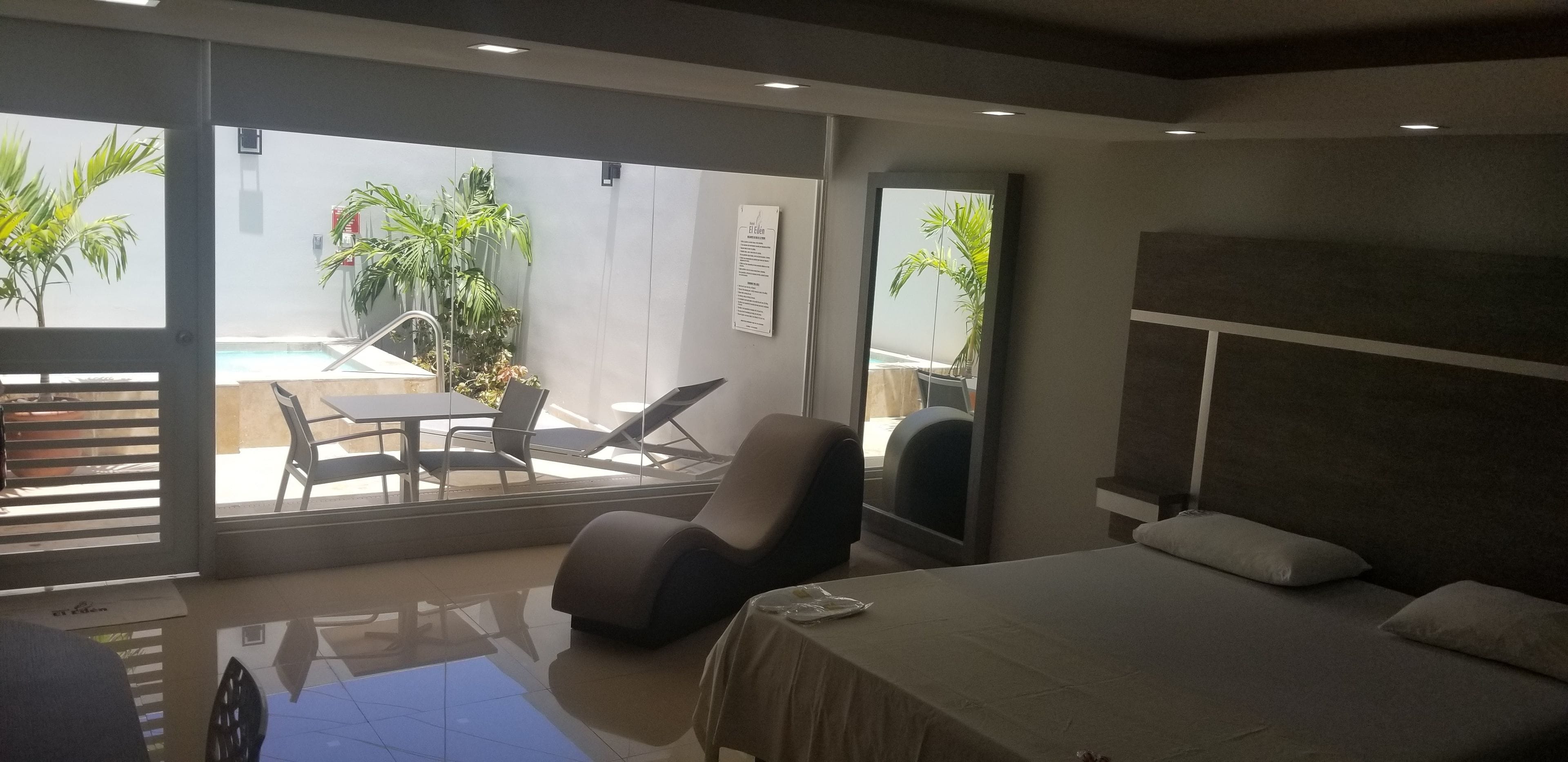 A modern hotel room with a bed, a desk, and a view of a pool and palm trees.