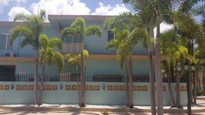 Um edifício de dois andares com fachada azul clara, varanda no andar superior e um painel decorativo com padrões geométricos.