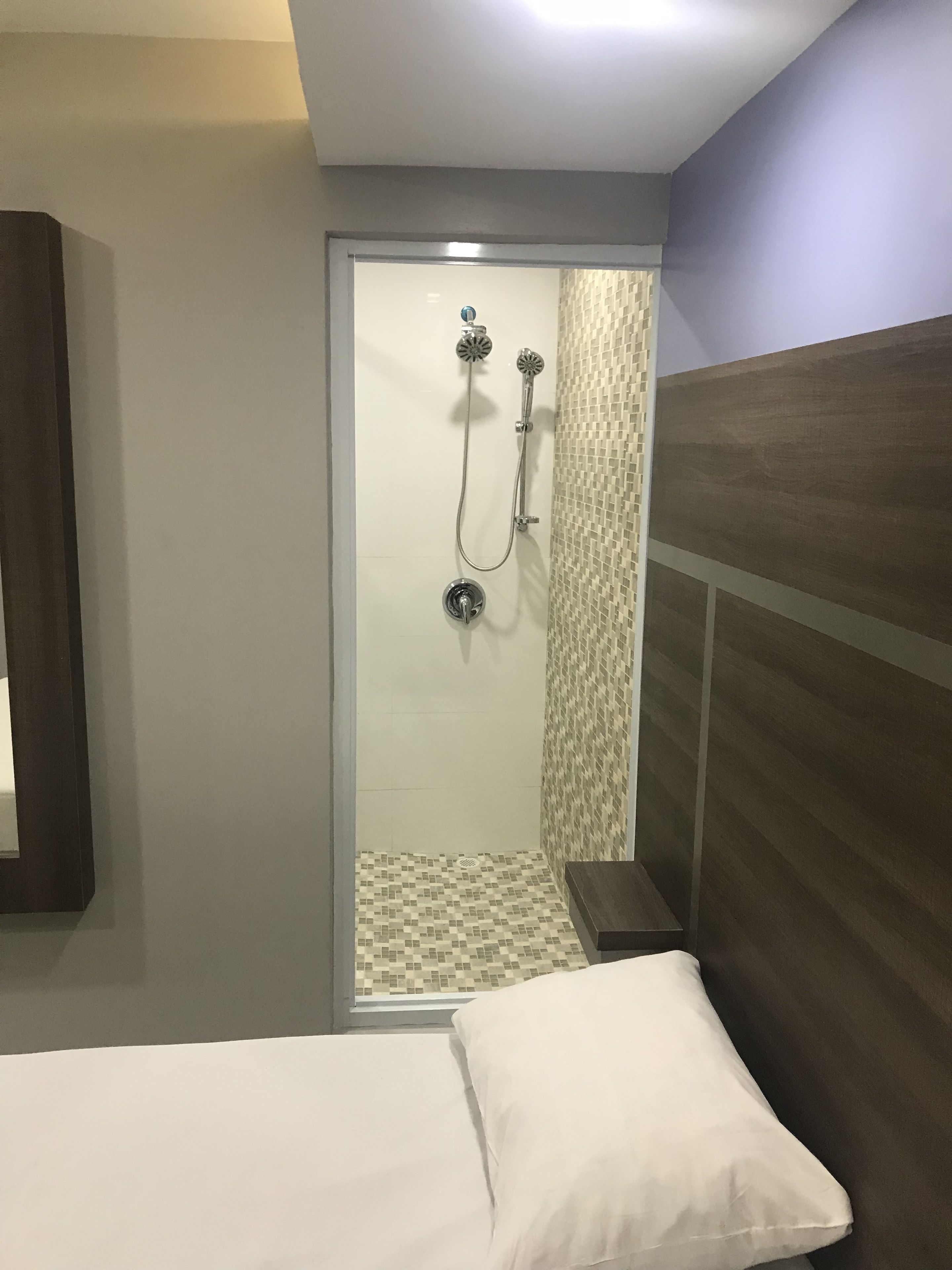 A hotel room with a shower, a bed with white bedding, and a wooden headboard.