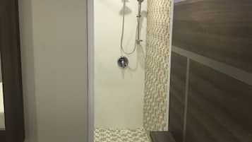 A hotel room with a shower, a bed with white bedding, and a wooden headboard.