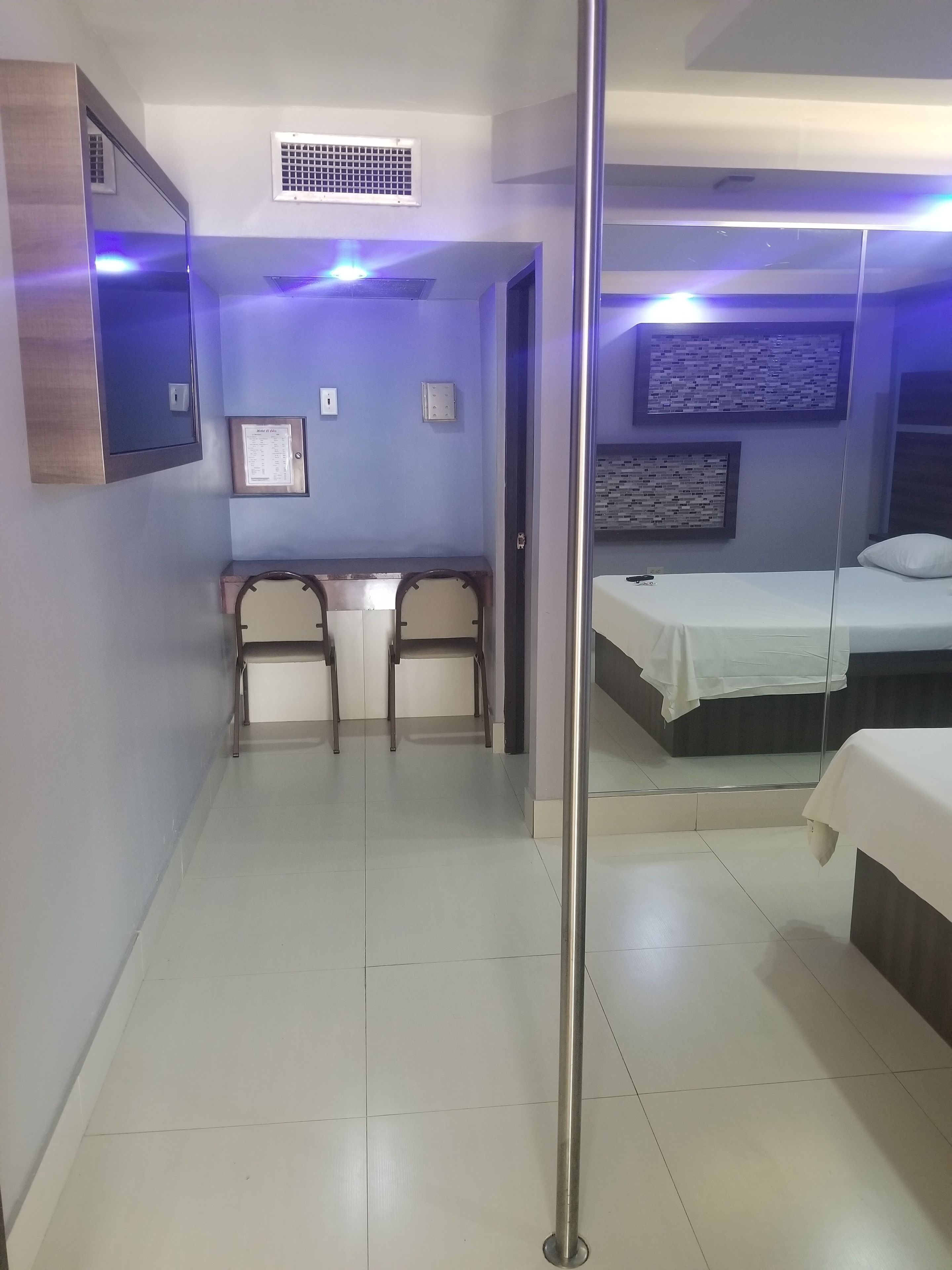 Une chambre d’hôtel avec un lit, un bureau avec des chaises, un miroir et une grille d’aération au mur.