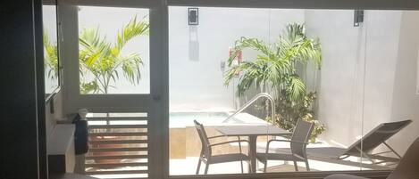 A modern room with a large sliding glass door leading to an outdoor area. Inside, there is a sofa, a chair, and a small table.